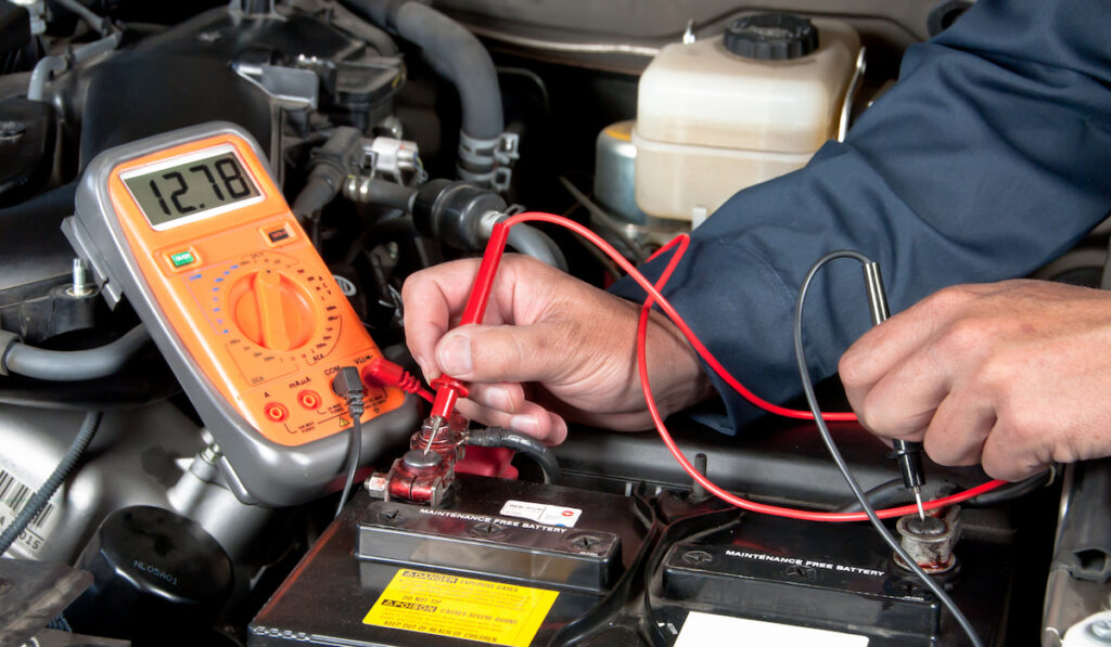 Auto mechanic uses a multimeter voltmeter checking voltage level in a car battery