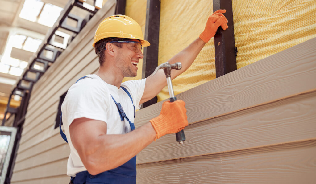 Happy male builder using hammer building  wood siding