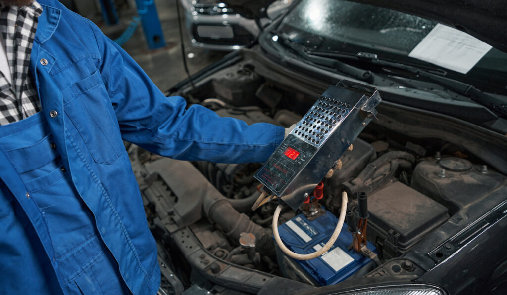 Mechanic in blue clothes holding load plug use for checking car battery
