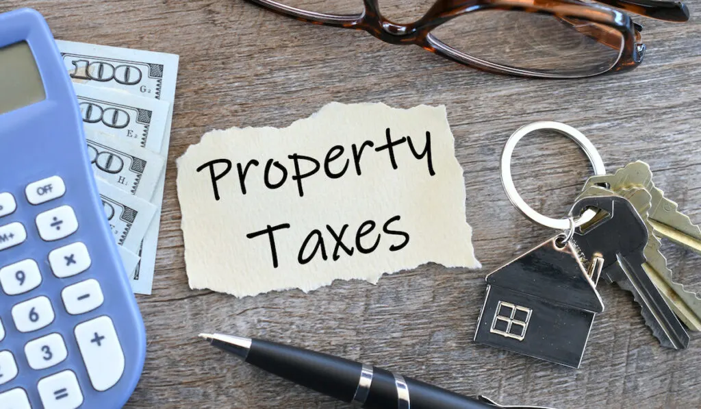 Paper that says Property Taxes with house keys calculator cash money reading glasses and ink pen