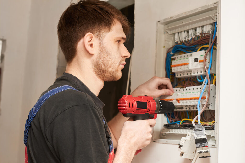 electrician builder engineer screwing equipment in fuse box